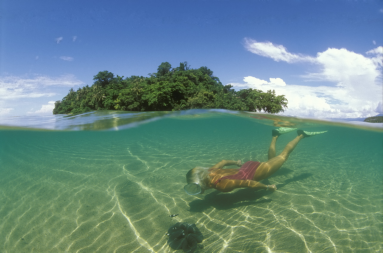 Une plongeuse observant une anémone de mer devant un îlot - Papouasie-Nouvelle Guinée