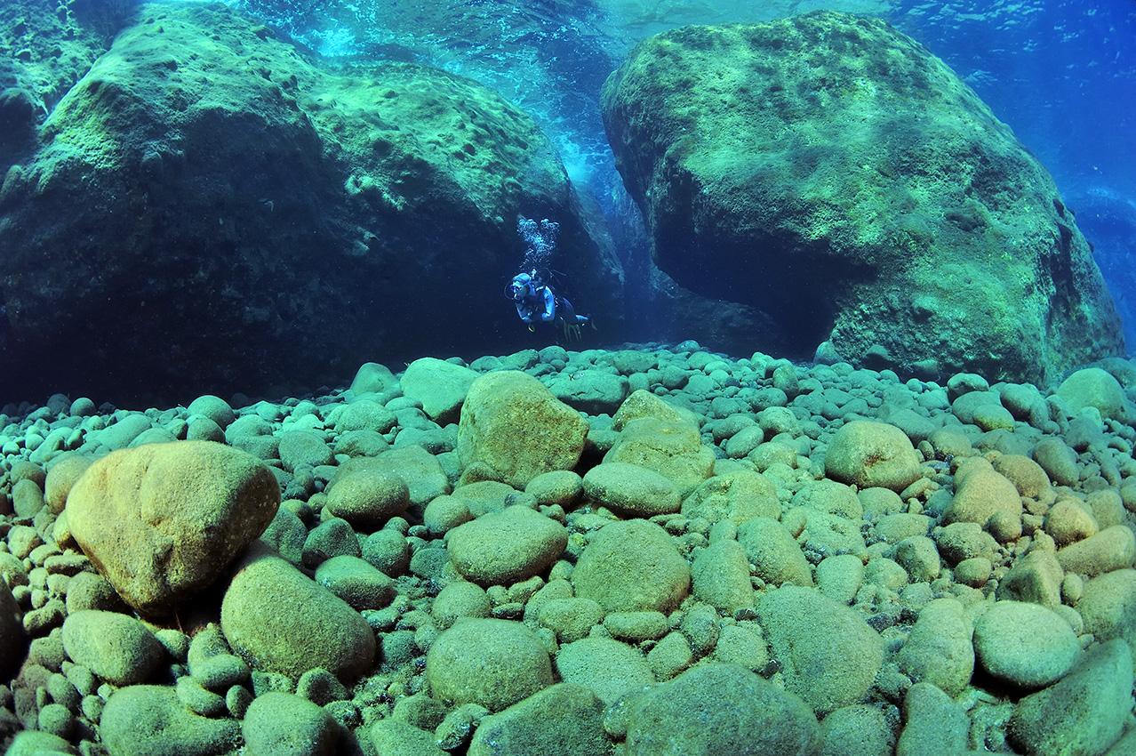 Un plongeur dans une zone de structures et grottes constituée de morceaux de lave - Grèce