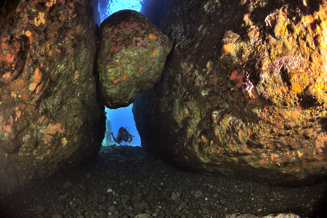 Un plongeur dans une zone de structures et grottes constituée de morceaux de lave - Grèce