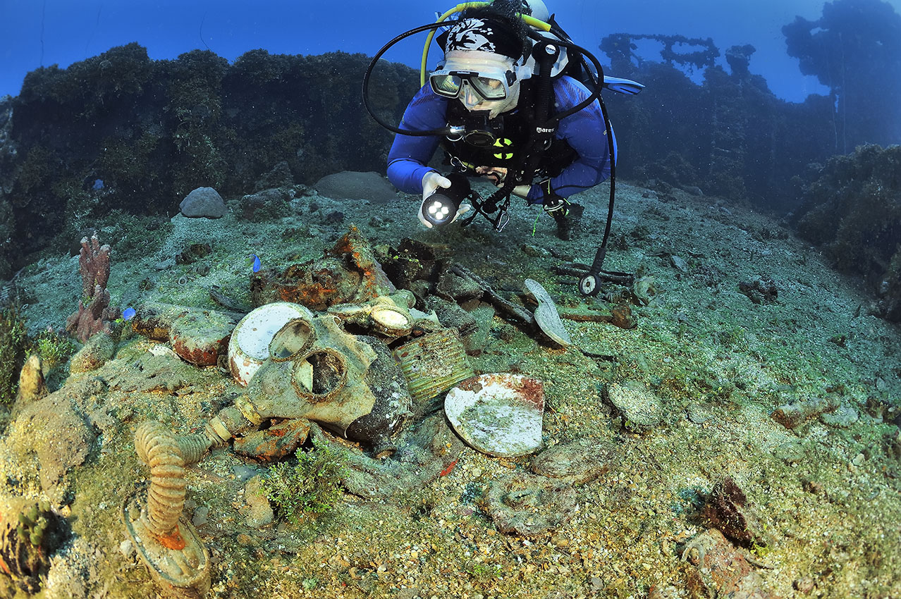 Une plongeuse éclaire divers débris dont des masques sur l'épave du Unkai Maru - Chuuk Lagoon ou Truk Lagoon